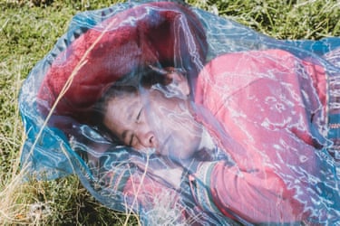 A person in Andean dress sleeps in field under diaphanous fabric