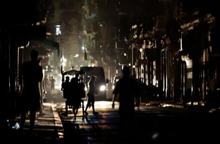 The headlights of a van light up people crossing a street during a blackout