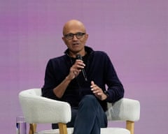 A man speaks into a microphone while seated onstage
