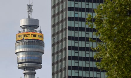 The top of the BT tower seen nest to a neighbouring skyscraper, with its circular messaging board displaying the message ‘Protect the NHS’ against a bright yellow background