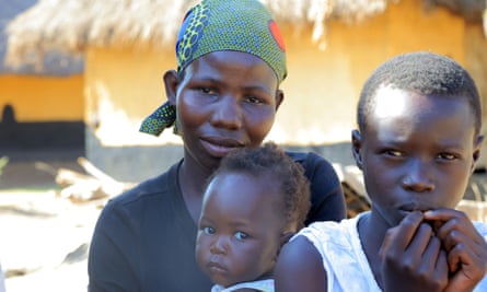 A woman wearing. a green headscarf holds a baby, while an older child stands in front of her