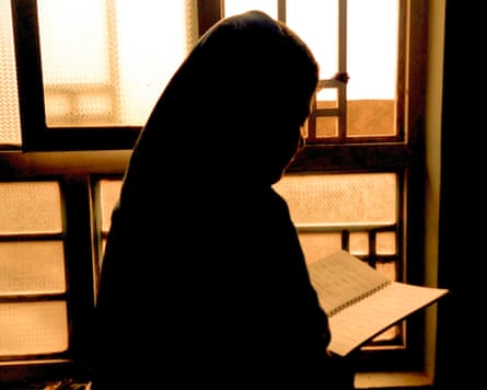 An Afghan woman in a headscarf reading from a notebook