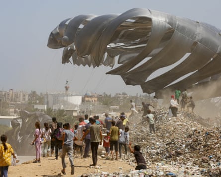 People move towards an aid drop landing under a silver parachute