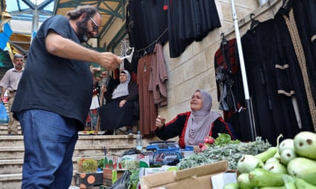 Kattan in navy T-shirt and jeans talks to Un Nabil in a lilac headscarf at a fruit and vegetable stall.