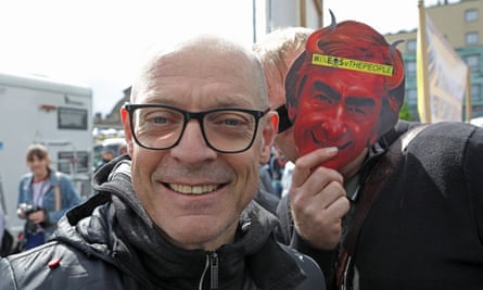 Sir Dave Brailsford with a protester wearing a mask of Jim Ratcliffe with devil horns.