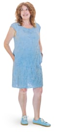 Gilli in pale blue dress and shoes, standing with a smile and hands in pockets