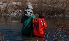 two people, one of whom is holding a child, cross a body of water