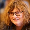 A woman with curly red hair and glasses, wearing a grey sparkly top