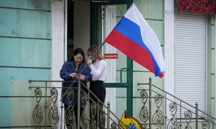 Women hang a Russian flag at their shop in Luhansk, one day after voting in four Moscow-held regions of Ukraine on referendums to become part of Russia.