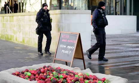 Police officers walk past 1,071 plastic ‘rotten apples’ outside New Scotland Yard, London, 20 January.