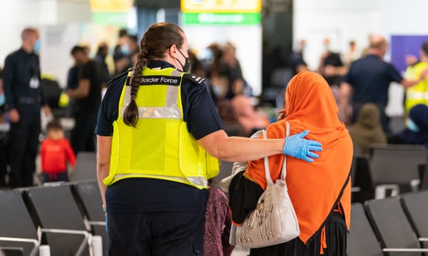 A member of Border Force staff assists a female evacuee as refugees arrive from Afghanistan at Heathrow Airport on August 26, 2021