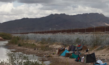 Migrants build makeshift tents with blankets to protect themselves from the cold, especially icy winds, as an American helicopter guards the border in Ciudad Juarez, Mexico on March 26, 2024, in the vicinity of the Rio Grande.