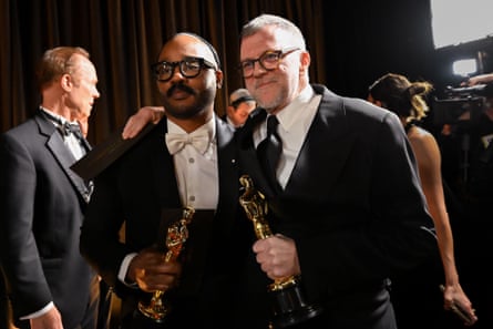 two men in suits and glasses holding their Oscar awards while posing together