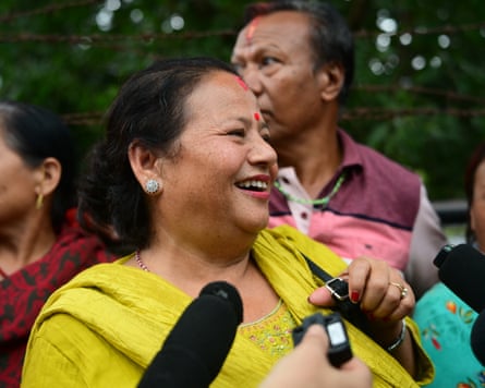 A smiling woman speaks as microphones are pointed towards her