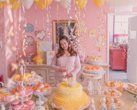 A woman holding her stomach in a pink-painted room filled with streamers and cakes and balloons