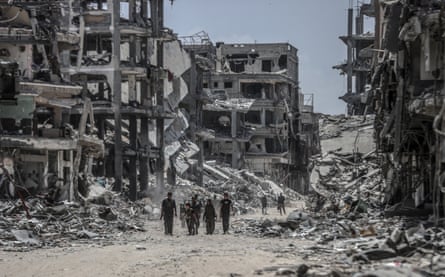 A group of people walk along a path between buildings that have been heavily bombed