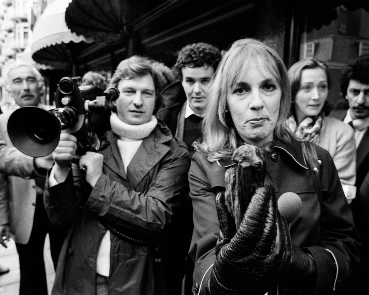 Esther Rantzen holding a microphone, with a crowd and a cameraman near her