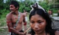 A Munduruku Indian woman warrior carries a monkey on her head, with other people from her tribe in. the background, Para state, Brazil.