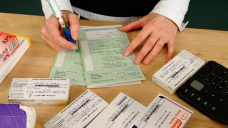 A pharmacist goes through NHS prescriptions at a desk with medication and a calculator on it