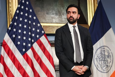 a man in a suit stands with his hands clasped