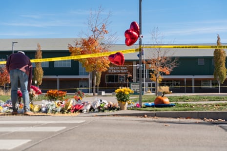 A man bends over a floral memorial beneath police tape outside Silver Rail Elementary School