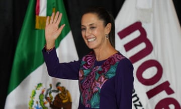 Claudia Sheinbaum waves at supporters with the Mexican flag in the background