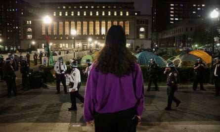 A protester looks on as the police stand guard near an encampment on the grounds of Columbia University.