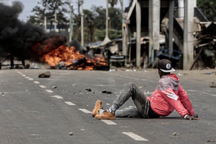 A protester lies in the road watching a burning tyre pile down the road