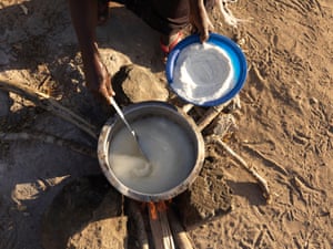 A woman spoons maize flour into water on a fire to make porridge