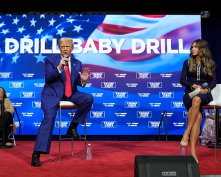 Donald Trump sitting on a chair speaking to the audience with ‘Drill baby drill’ written on a screen behind him