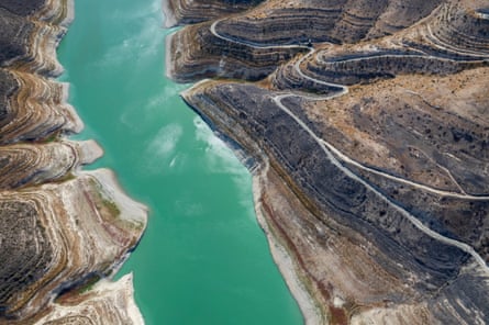 Aerial view of Kouris dam with a narrow strip of green-blue water between brownish rocks.
