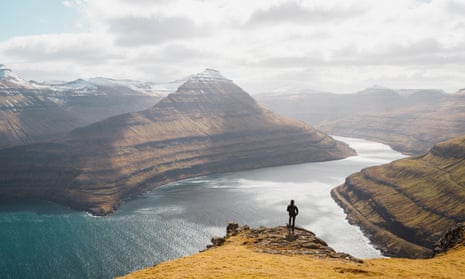 Lonely hiker enjoying the view over spectacular Faroese fjords near Funningur during a sunny spring morning 