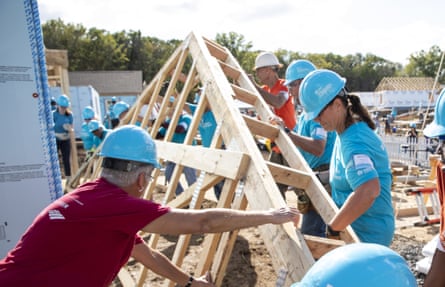 People in blue hard hats hold up a wooden structure