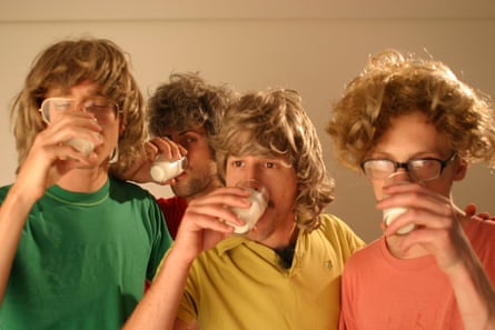 Four men wearing brightly coloured T-shirts and blond wigs each drink milk from a glass.