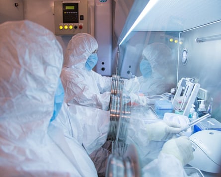 Two technicians in hazmat suits with their arms in a isolator chamber