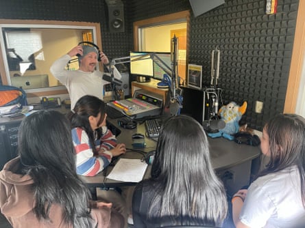 A man in a radio station stands in front of a microphone while speaking to kids sitting in front of him
