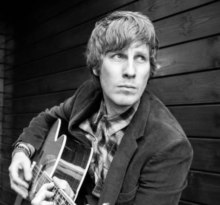 Folk artist Scott Matthews playing his guitar while looking away from camera.