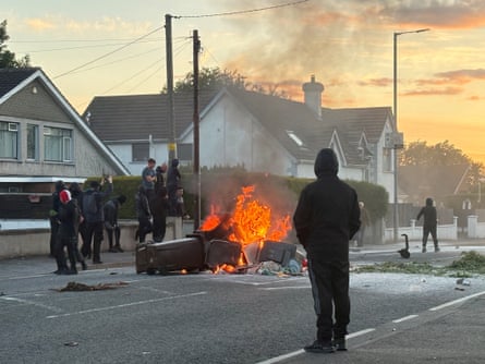 Black-clad protesters watching a burning vehicle in Belfast.