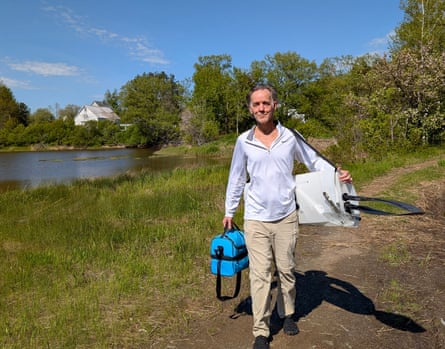 man holding a cooler and foldable kayak while walking on path beside water