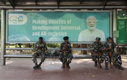 Paramilitary soldiers sit at a bustop displaying an advertisement of the G20 Summit.