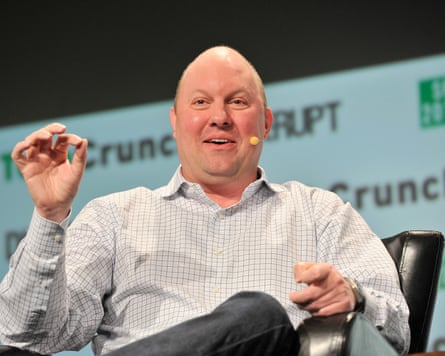 He sits in a black chair on stage, wearing a microphone and gesticulating with his right hand