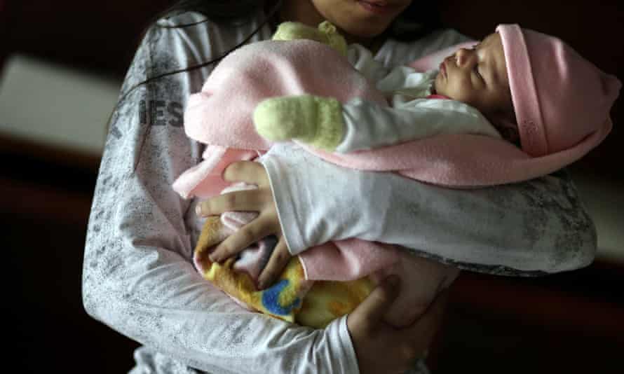 パラグアイの避難所で13歳の女の子が赤ちゃんを抱いています。