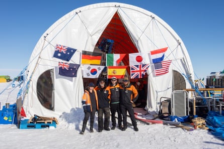A group of people standing outside the SWAIS2C camp in the snow, with flags from different countries hung over the entrance