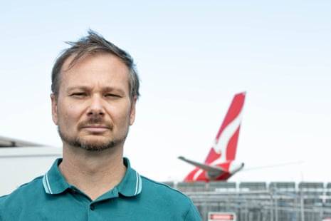 A man wearing a green shirt and a disgruntled expression, with a Qantas plane in the background