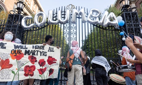 Silver balloons spell out Columbia at top of black iron gate, and people hold sign with red flowers that says We Will Honor All Our Martyrs.