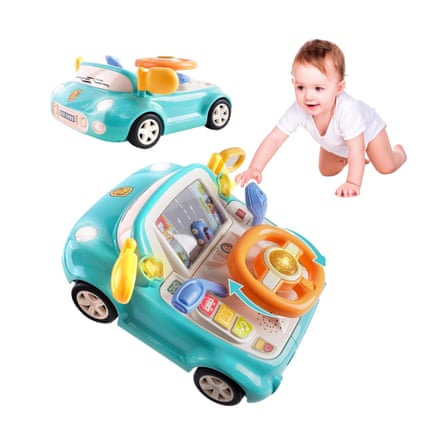 A baby crawls towards a teal interactive toy driving car with a steering wheel and screen