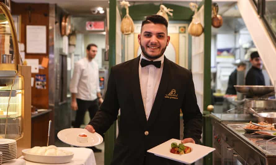Young male waiter holding two plates of food and smiling at the camera at Mimí alla Ferrovia, Naples, Italy.