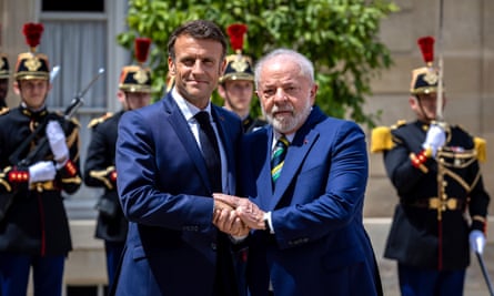 two men in suits holding hands closely with people in ceremonial military dress behind them