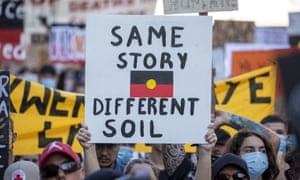 A protester holds a placard depicting the Australian Aboriginal Flag.