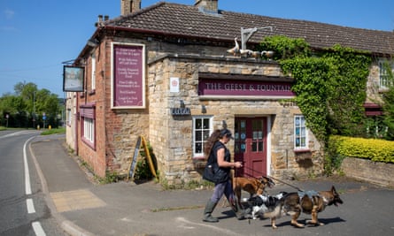 Seorang wanita dan tiga anjing berjalan di depan Geese and Fountain Pub, dekat Grantham, yang akan tutup pada hari Senin menyusul permintaan sewa yang tinggi.